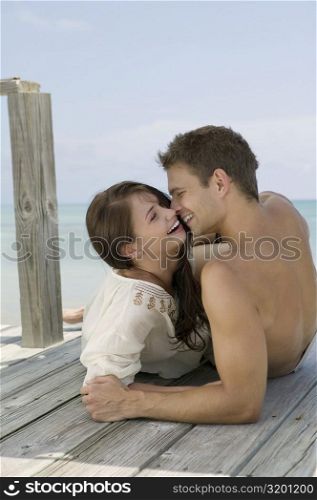 Close-up of a young couple lying on a pier and looking at each other