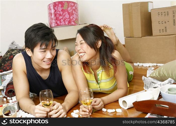 Close-up of a young couple lying on the floor and holding glasses of wine