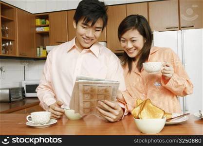 Close-up of a young couple reading a newspaper at a kitchen counter