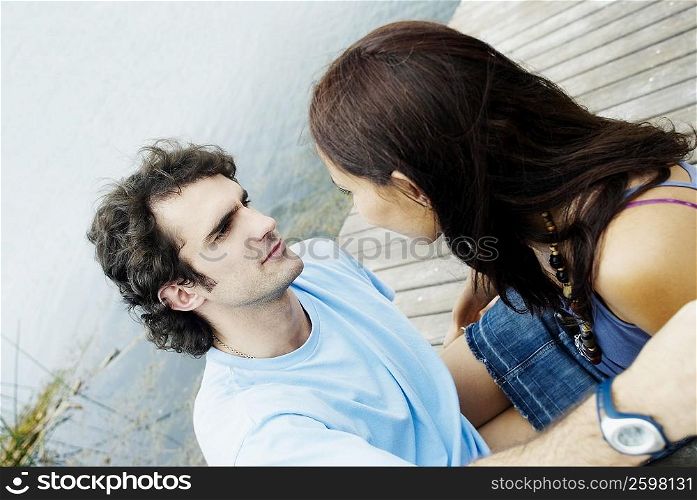 Close-up of a young couple sitting at a pier and looking at each other