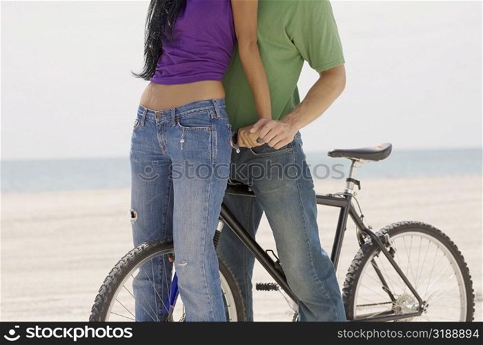 Close-up of a young couple standing on the beach with a bicycle