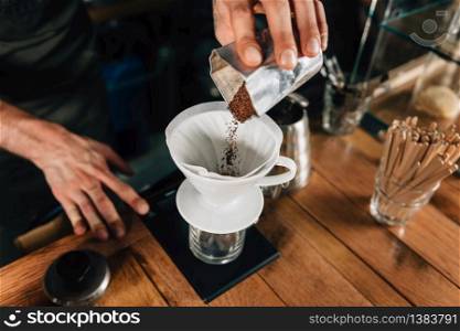 Close up of a young male barista hands pouring coffee into ceramic glass and measure it on digital scale in coffee shop. Barista wearing dark uniform. Tools and equipment for making Drip Brew coffee on wooden table.