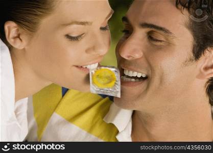 Close-up of a young man and a teenage girl holding a condom between her teeth
