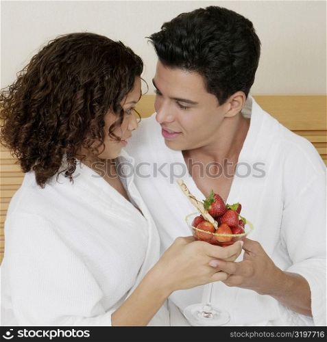 Close-up of a young man and a teenage girl holding a glass of strawberries