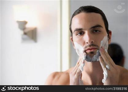 Close-up of a young man applying shaving cream on his face
