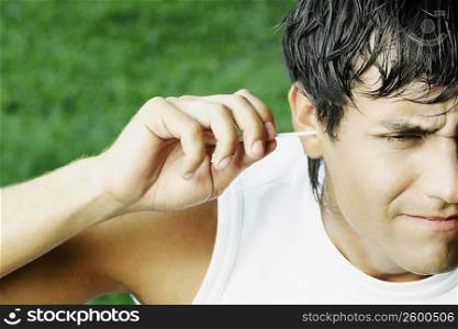 Close-up of a young man cleaning his ear with a cotton swab