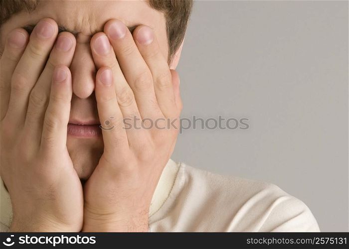 Close-up of a young man covering his eyes with his hands