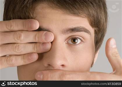 Close-up of a young man covering his mouth and his eye with his hands