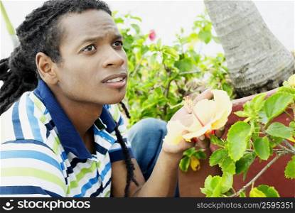 Close-up of a young man crouching and touching a flower