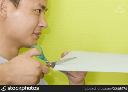 Close-up of a young man cutting a paper with scissors