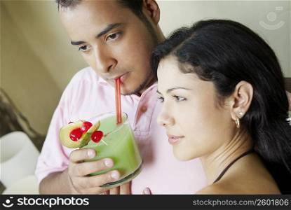 Close-up of a young man drinking juice with a young woman beside him