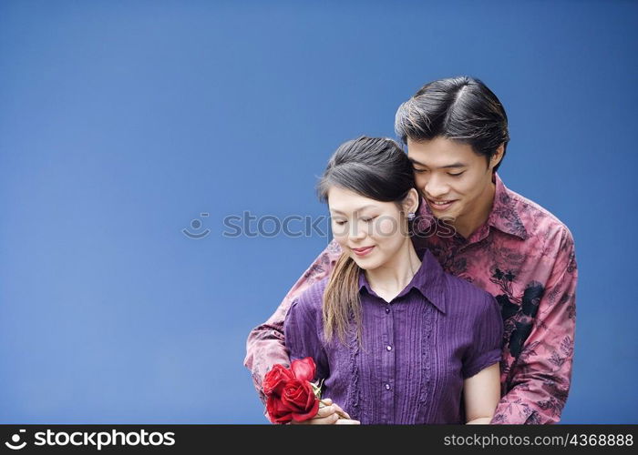 Close-up of a young man embracing a young woman from behind and holding roses