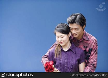Close-up of a young man embracing a young woman from behind and holding roses
