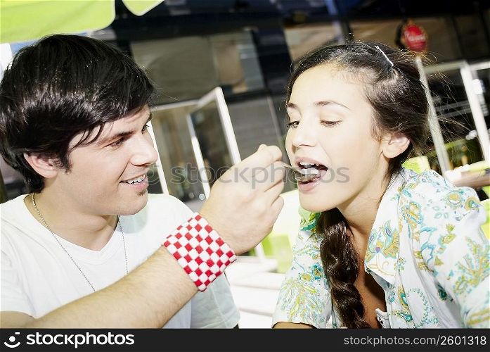 Close-up of a young man feeding ice-cream to a young woman