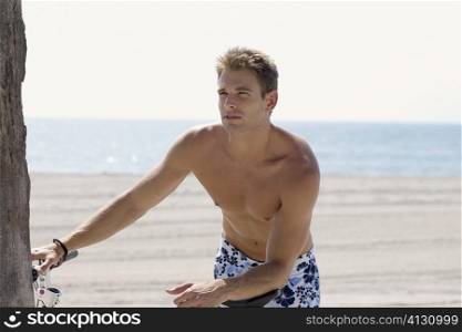 Close-up of a young man holding a bicycle on the beach