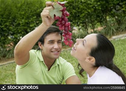 Close-up of a young man holding a bunch of grapes with a young woman eating it
