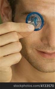 Close-up of a young man holding a condom in front of his eye