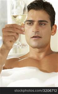 Close-up of a young man holding a glass of white wine in a bathtub