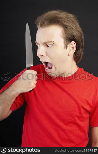 Close-up of a young man holding a knife and looking scared