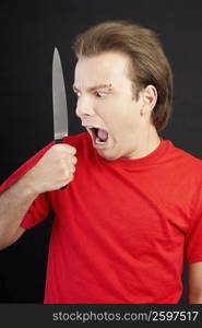 Close-up of a young man holding a knife and looking scared