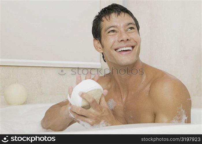 Close-up of a young man holding a loofah in a bathtub