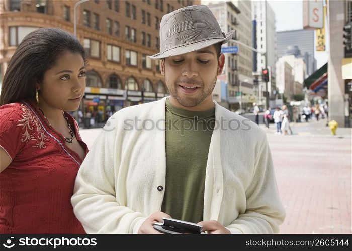 Close-up of a young man holding a personal data assistant with a young woman looking at him