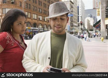 Close-up of a young man holding a personal data assistant with a young woman looking at him