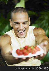 Close-up of a young man holding a plate of strawberries and smiling