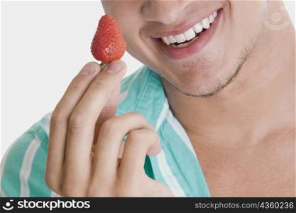 Close-up of a young man holding a strawberry and smiling