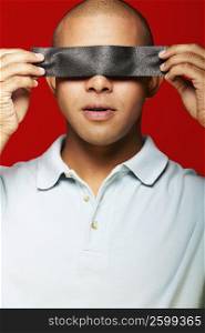 Close-up of a young man holding duct tape in front of his eyes