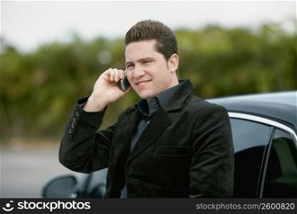 Close-up of a young man leaning against a car and talking on a mobile phone