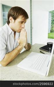 Close-up of a young man looking at a laptop and thinking