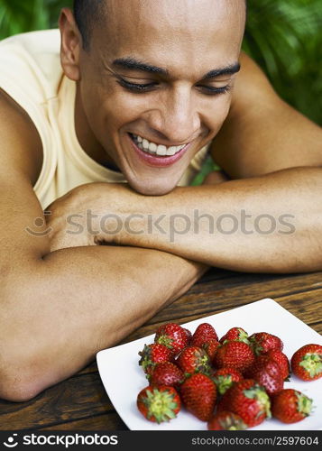 Close-up of a young man looking at a plate of strawberries and smiling