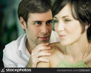 Close-up of a young man looking at a young woman with his hand on her shoulder