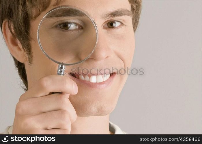Close-up of a young man looking through a magnifying glass