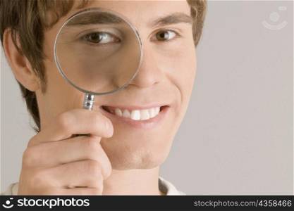 Close-up of a young man looking through a magnifying glass