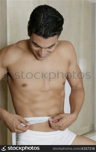 Close-up of a young man measuring his waist with a tape measure