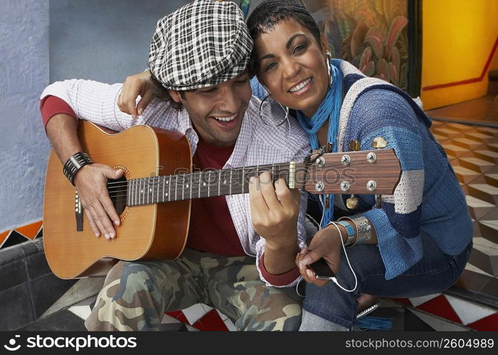 Close-up of a young man playing a guitar and smiling with a young woman