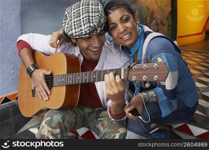 Close-up of a young man playing a guitar and smiling with a young woman