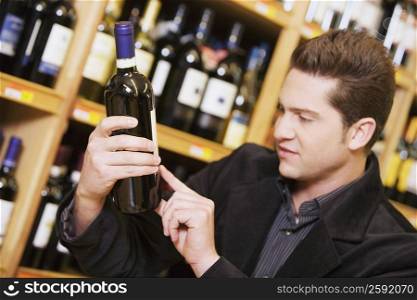 Close-up of a young man reading a label of a wine bottle in a liquor store