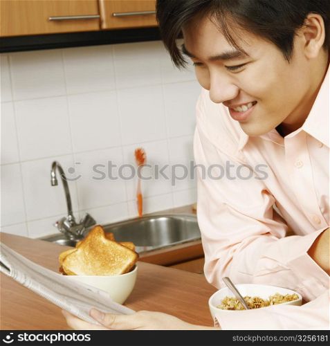 Close-up of a young man reading a newspaper at a kitchen counter