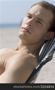 Close-up of a young man resting on a chair on the beach
