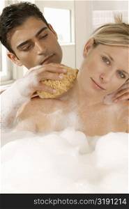 Close-up of a young man scrubbing a young woman&acute;s neck with a bath sponge