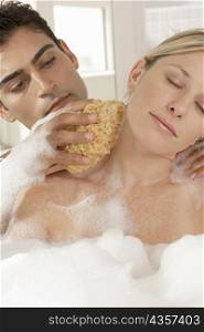Close-up of a young man scrubbing a young woman&acute;s neck with a bath sponge