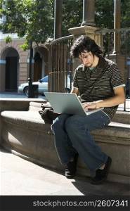Close-up of a young man sitting and using a laptop