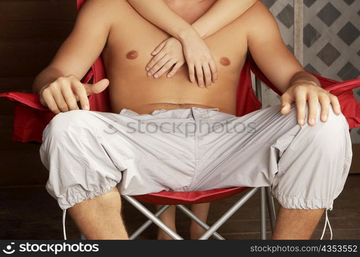 Close-up of a young man sitting in an armchair with a young woman embracing him from behind
