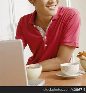 Close-up of a young man smiling in front of a laptop at a kitchen counter