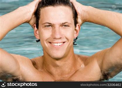 Close-up of a young man smiling with his hands behind his head in a swimming pool