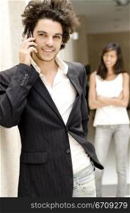 Close-up of a young man talking on a mobile phone with a young woman standing behind him