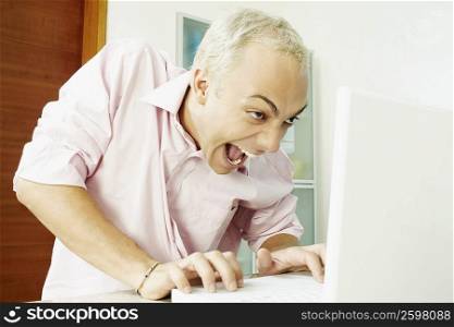 Close-up of a young man using a laptop and making a face